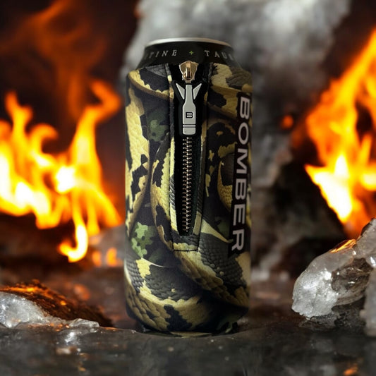 Bomber Venom AI Snake 16oz zippered 4mm neoprene can insulator in olive green camo snake print beside a campfire with ice