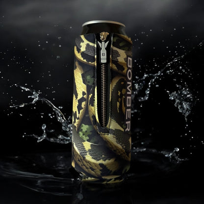 A slim aluminum can wrapped in a black, tan, and green snake-print zipper sleeve with the word BOMBER printed vertically, shown against a dark background with water splashes.