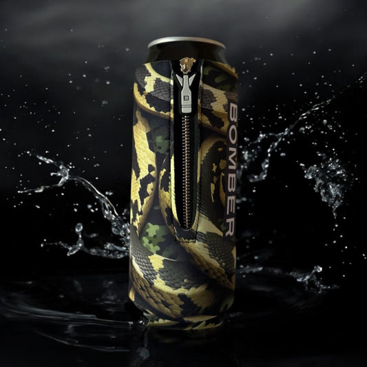 A slim aluminum can wrapped in a black, tan, and green snake-print zipper sleeve with the word BOMBER printed vertically, shown against a dark background with water splashes.