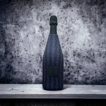 A dark blue patterned champagne bottle with a black foil top, standing on a light gray stone ledge against a textured gray and white speckled background.