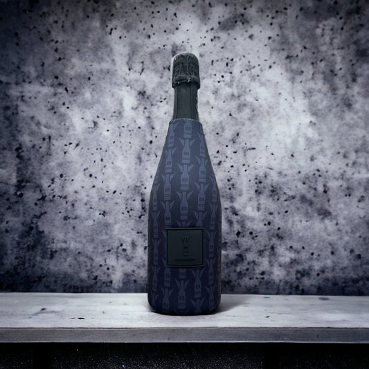 A dark blue patterned champagne bottle with a black foil top, standing on a light gray stone ledge against a textured gray and white speckled background.